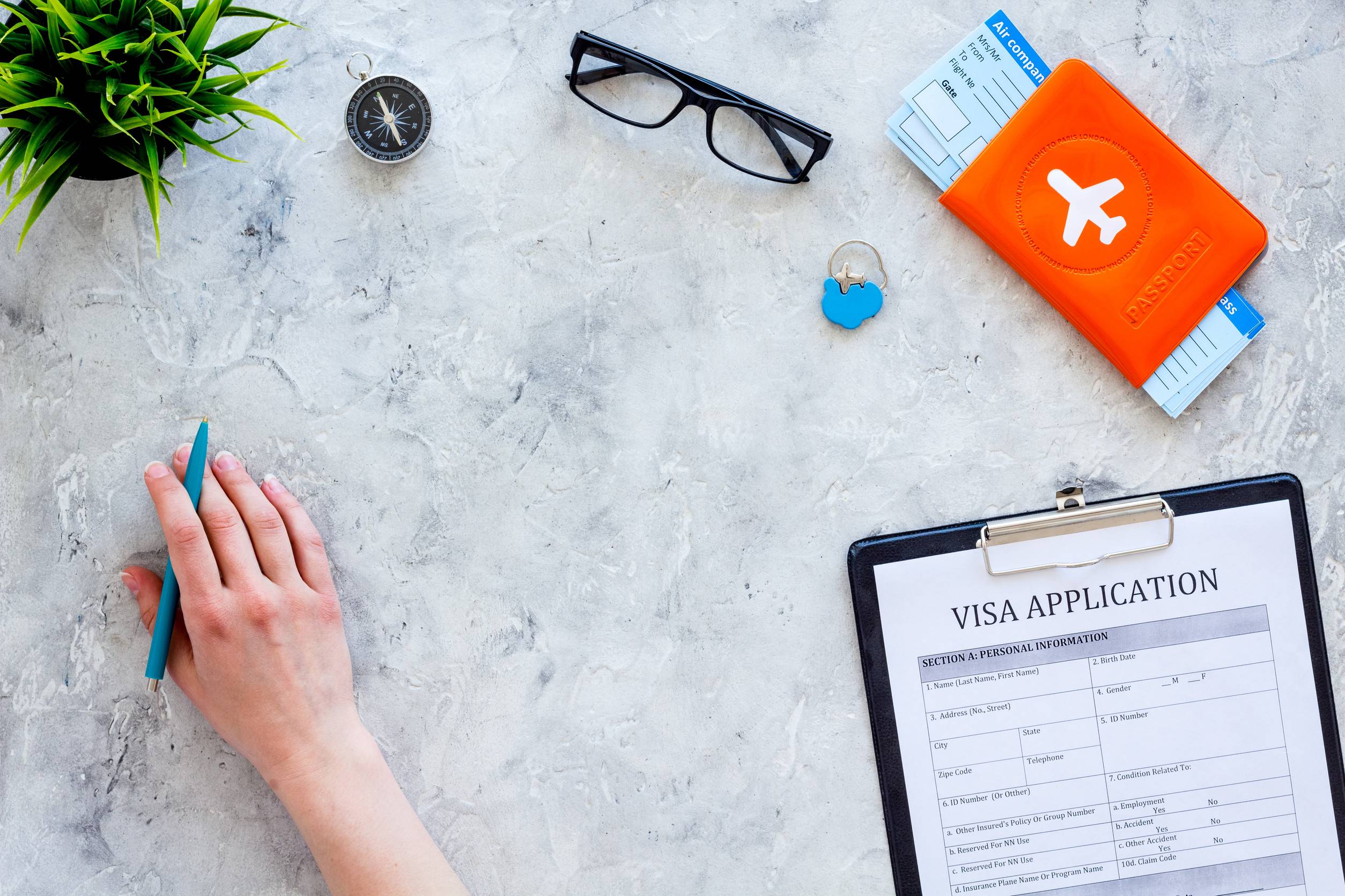 hand filling visa application form near glasses pen passport