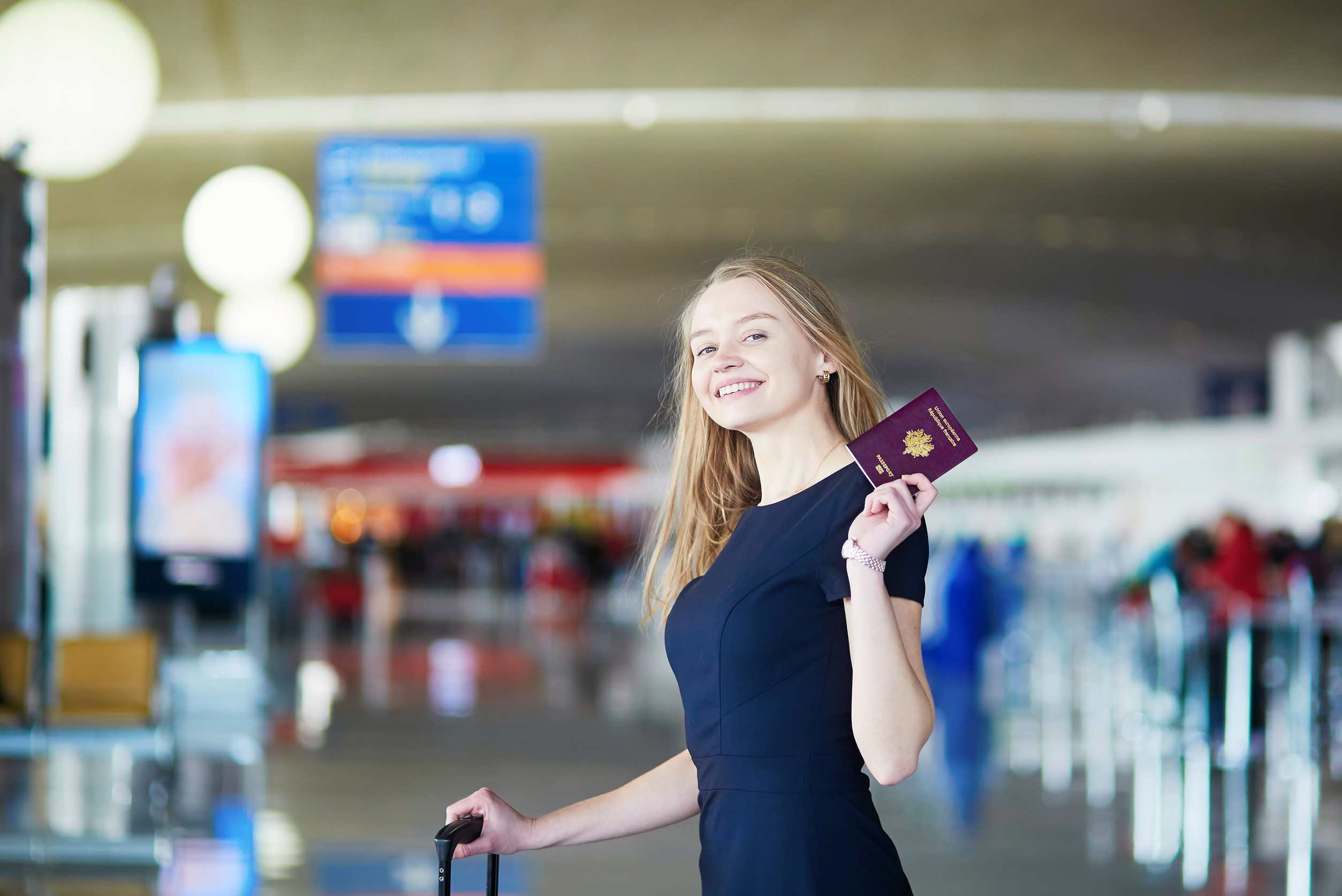 young woman in international airport holding french passport and looking happy